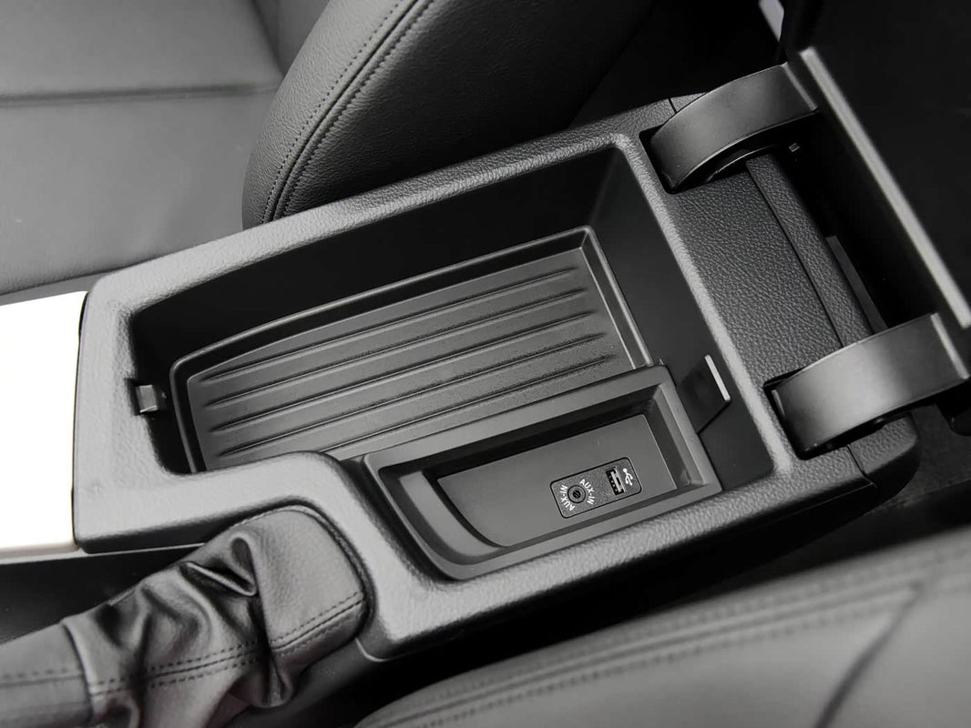 An open car armrest storage compartment, revealing an AUX-in port and a USB port, indicating connectivity options within the vehicle
