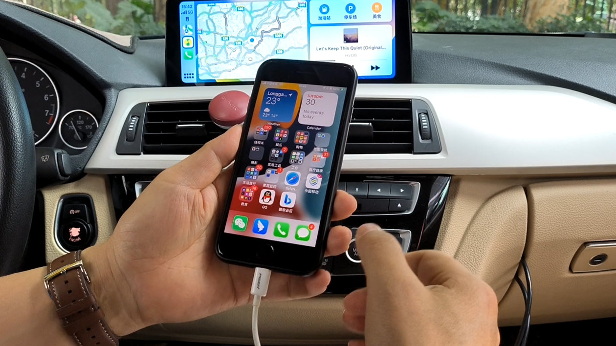 Person holding an iPhone in a car, with CarPlay on the dashboard screen.